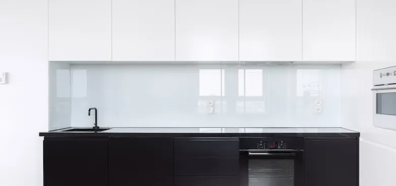 Crédence en verre laqué blanc posée entre le plan de travail et les meubles hauts d'une cuisine