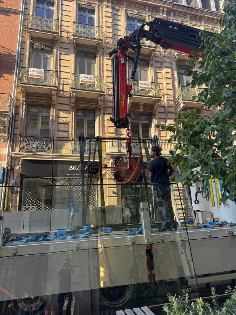 Le vitrage sanglé sur le plateau du camion, saisi par le palonnier à ventouses avant le levage