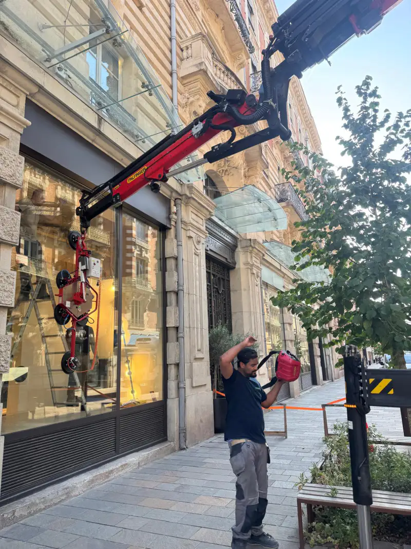 Opérateur pilotant la grue à la radiocommande, palonnier à ventouses suspendu devant la devanture
